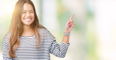 Kameraya bakarak yan el ve parmak ile işaret yüzünde kocaman bir gülümseme ile izole arka plan üzerinde çizgili süveter giyen genç güzel esmer kadın.