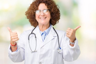 Orta ager kıdemli doktor kadın izole arka plan başarı işareti başparmak gülümseyen ve mutlu el ile olumlu hareketi yapıyor. Neşeli bir ifadeyle, kazanan jest kameraya bakıyor.