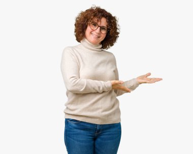 Güzel orta ager kıdemli kadın giyen balıkçı yaka kazak ve gözlük üzerinde izole arka planda açık el ile gülümseyen doğal girmek için davet