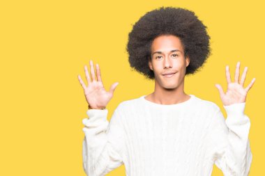 Afro saç içeren genç Afrikalı Amerikalı adam kış kazak gösteren ve parmak numarası on ile işaret kadar güven ve mutlu gülümseyen.