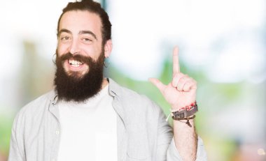 Uzun saç, sakal ve başarılı fikirle parmağı yukarıyı küpe olan genç adam. Çıktıktan ve mutlu. Bir numara.