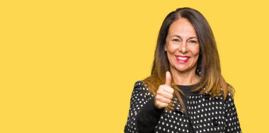 Güzel orta yaş kadın el ile jest kadar mutlu başparmak yapıyor moda ceket giyiyor. Başarı gösteren kameraya bakarak ifadeyi onaylama.