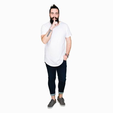 Uzun saç ve sakal dudaklarında parmak ile sessiz olmanı casual beyaz t-shirt giyen genç hipster adam. Sessizlik ve gizli kavramı.
