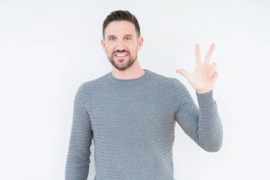 Soyutlanmış arka planda rahat bir süveter giyen genç yakışıklı üç numaralı parmaklarıyla gülümseyerek kendinden emin ve mutlu bir şekilde onu işaret ediyor..