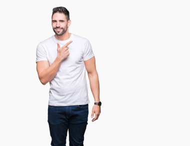 İzole arka neşeli bir gülümseme ile yüz el ve parmak kadar mutlu ve doğal ifade yüzünde yanında işaret içinde Casual beyaz t-shirt giyen genç adam