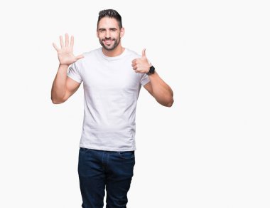 Gösterilen ve parmakları ile işaret izole arka plan üzerinde rahat beyaz t-shirt giyen genç adam kendinden emin ve mutlu gülümseyerek süre 6 numara.