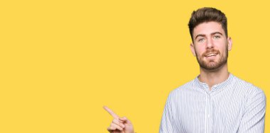 Kameraya bakarak yan el ve parmak ile işaret eden genç yakışıklı adam yüzünde kocaman bir gülümseme ile.