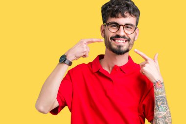 Kendinden emin gösterilen ve işaret parmakları diş ve ağız ile gülümseyen izole arka plan üzerinde gözlük takan yakışıklı delikanlı. Sağlık kavramı.
