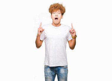 Casual beyaz t-shirt giyen afro saçlı yakışıklı delikanlı hayrete ve yukarıya bakıyor ve parmakları ile işaret ve silah kaldırdı şaşırttı.