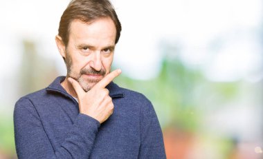 Orta yaş yakışıklı adam emin çapraz kollar ve çeneme kaldırdı el ile gülümseme ile kameraya bakarak bir kazak giyiyor. Pozitif düşünce.