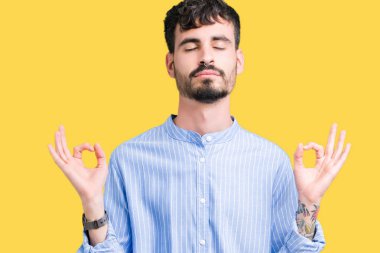 Genç yakışıklı iş adamı izole arka plan üzerinde dinlenmek ve gülümseyen gözlerle kapalı parmak jestle meditasyon yapıyor. Yoga kavramı.