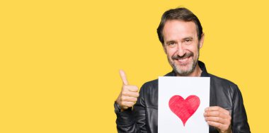 Ok işareti, başparmak ile parmak, mükemmel işareti yapıyor kocaman bir gülümseme ile kağıt kırmızı kalp ile mutlu tutmak yakışıklı orta yaş erkek