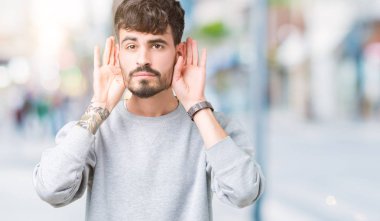 Her ikisi de dinliyoruz izole arka plan üzerinde sweatshirt giyen genç yakışıklı adam kulak jest, dedikodu için meraklı eller. İşitme sorunu, sağır