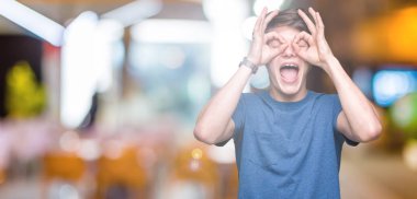 Dilini, parmaklarının arasından baktığını yapışmasını dürbün gibi ok jest yapıyor izole arka plan üzerinde mavi t-shirt giyen genç yakışıklı adam. Deli ifade.