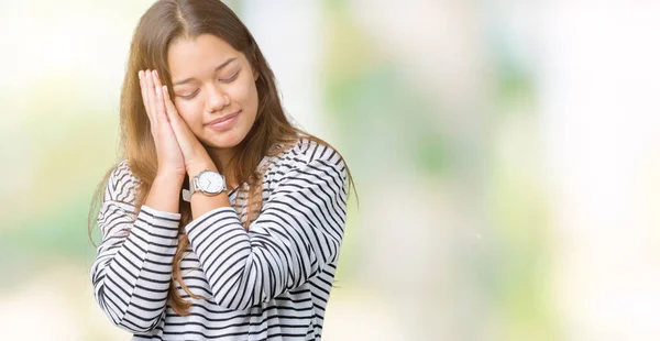 年轻美丽的黑发女人穿着条纹毛衣在孤立的背景睡累的梦和摆姿势双手在一起 而微笑着闭着眼睛 — 图库照片