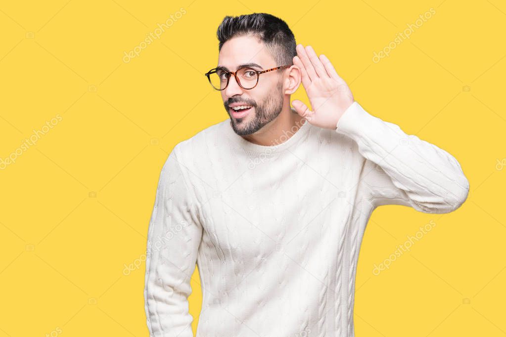 Young handsome man wearing glasses over isolated background smiling with hand over ear listening an hearing to rumor or gossip. Deafness concept.