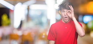 Sürpriz yüz, göz parmaklarının arasından seyir ile ok jest yapıyor izole arka plan üzerinde kırmızı t-shirt giyen genç yakışıklı adam şok. İmansız ifade.