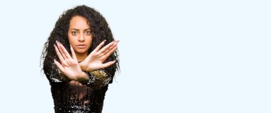 Gece partisi elbise giyen kıvırcık saçlı Genç güzel kız ret ifadesi geçiş silah ve avuç içi negatif işareti, öfkeli yüz yapıyor