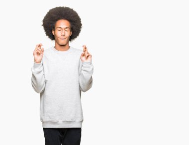 Afro saç ile genç Afrikalı Amerikalı adam sportif Sweatshirt gülümseme geçiş parmaklar ile umut ve gözleri kapalı. Şans ve batıl fikir.