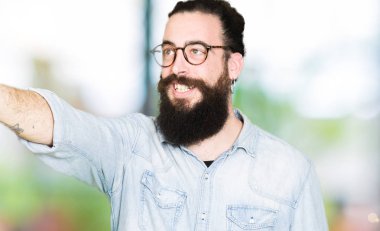 Uzun saç ve sakal giyen genç hipster adamla gözlük işaret parmağı ile devam sürpriz, açık ağız hayret ifadesi, önünde bir şey