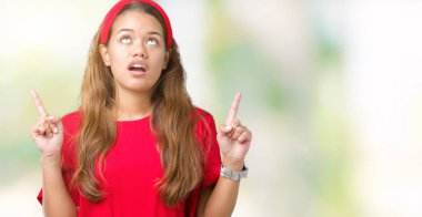 İzole arka plan üzerinde kırmızı t-shirt giyen genç güzel esmer kadın hayrete ve yukarıya bakıyor ve parmakları ile işaret ve silah kaldırdı şaşırttı.