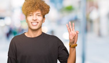 Afro saç ile genç yakışıklı adam siyah t-shirt gösteren ve parmak sayısı üç ile işaret kadar kendine güvenen ve mutlu gülümseyen.