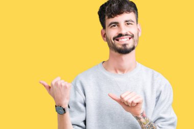Yakışıklı delikanlı üzerinde sweatshirt giyen izole arka plan emin gülümseyen arkasından el ve kadar başparmak ile işaret