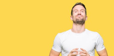 Yakışıklı adamın Casual beyaz t-shirt eller birlikte giydiğini ve parmakları rahat ve neşeli gülümseyen geçti. Başarı ve iyimser