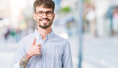 Hareketi el ile mutlu yaşasın yapıyor izole arka plan üzerinde gözlük takan yakışıklı delikanlı. Kameraya bakarak başarı gösteren ile ifade onaylama.