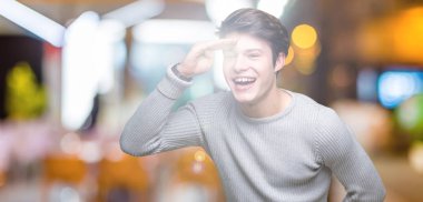 Üzerinde kış kazak giyen genç yakışıklı adam arka plan çok mutlu ve gülümseyen uzakta el ile üzerine kafa seyir izole. Arama kavramı.