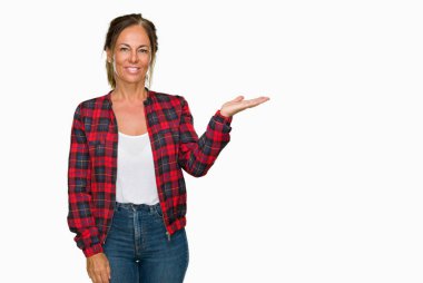 Neşeli sunulması ve kameraya bakarak avucunun ile işaret gülümseyen izole arka plan üzerinde rahat ceket giyen orta yaş yetişkin kadın.