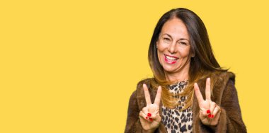 Güzel orta yaş zarif kadın vizon ceket giyen kamera parmaklar zafer işareti yapıyor gösteren bakıyor gülümseyen. İki numara.