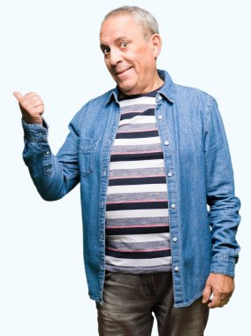 Yakışıklı kıdemli adam kot ceket giymiş mutlu yüz görünümlü ve başparmak ile yan işaret ile gülümseyen.