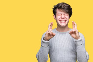 Geçiş parmakları umut ve gözleri kapalı ile gülümseyen izole arka plan üzerinde kış kazak giyen genç yakışıklı adam. Şans ve batıl kavramı.