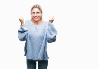 İzole arka plan üzerinde kutluyor kış kazak giyen genç güzel sarışın ve mavi gözlü kadın şaşırttı ve başarı için kaldırdı kollarını açarak hayret ve gözleri açık. Kazanan kavramı.