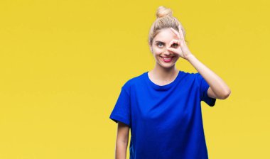 Gülümseyen, parmakları ile mutlu yüz üzerinden seyir göz el ile ok jest yapıyor izole arka plan üzerinde mavi t-shirt giyen genç güzel sarışın ve mavi gözlü kadın.