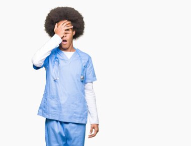 Yüz ve gözler el ile kapsayan şok bakmak afro saçlı genç Afro-Amerikan Doktor adam utanç ifadesi ile parmaklarımın arasından bakan.
