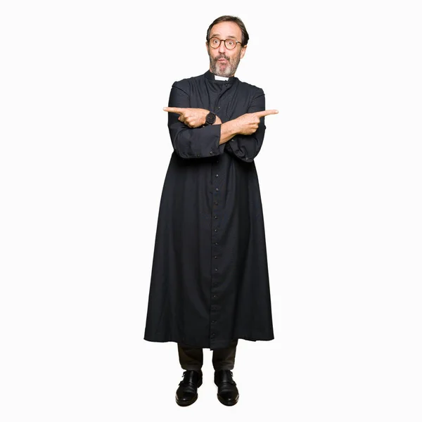 カトリックを着た中年僧侶男が指で両側にポインティングをローブ 別の方向に反対 — ストック写真
