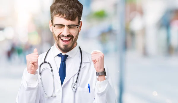 腕の成功のために興奮して孤立の背景の上病院コートを着た若い医師男は祝う勝利笑顔を発生します 勝者の概念 — ストック写真