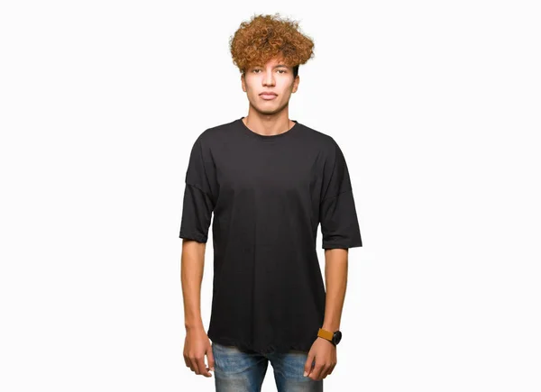 黒いTシャツを着たアフロヘアの若いハンサムな男は 真剣な表情でリラックスした表情 カメラを見てシンプルで自然な — ストック写真