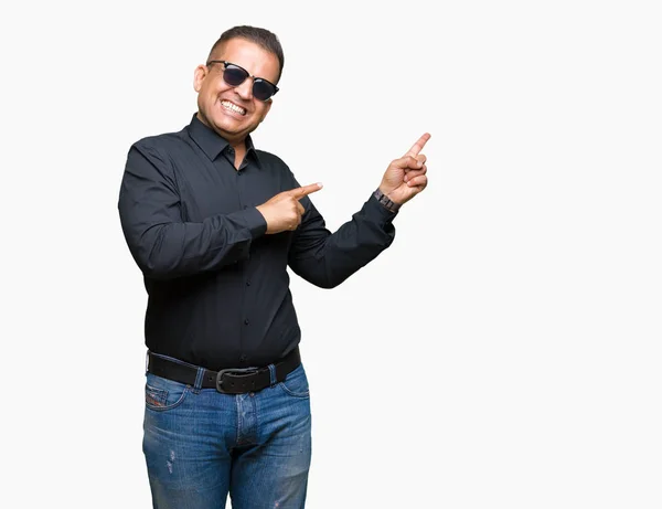 中年阿拉伯男子戴着太阳镜在孤立的背景微笑着 看着相机指向镜头 用两只手和手指指着一边 — 图库照片