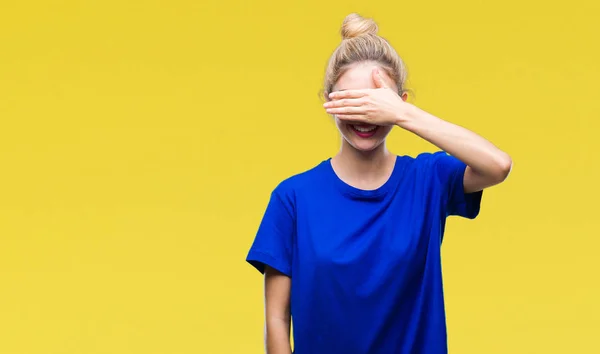 Young beautiful blonde and blue eyes woman wearing blue t-shirt over isolated background smiling and laughing with hand on face covering eyes for surprise. Blind concept.