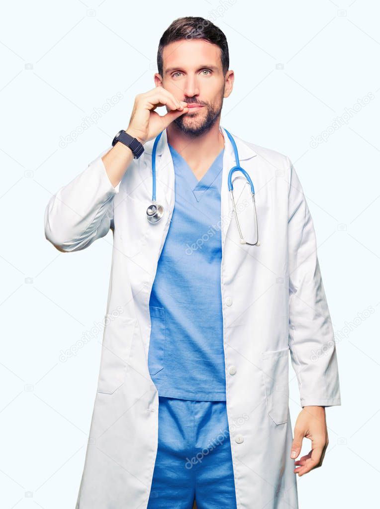 Handsome doctor man wearing medical uniform over isolated background mouth and lips shut as zip with fingers. Secret and silent, taboo talking