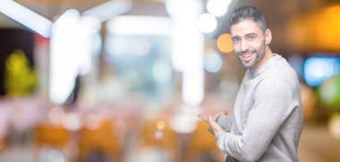 Açık el ile doğal gülümseyen girmek için davet izole arka plan üzerinde sweatshirt giyen genç yakışıklı adam