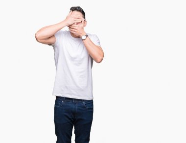 Beyaz izole arka plan üzerinde beyaz t-shirt giyen yakışıklı adam elleri ile gözleri ve ağız kaplama, şaşırttı ve şok. Duyguyu gizleme