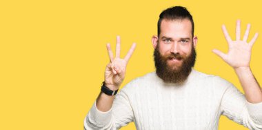 Kış kazak gösterme ve parmakları ile işaret giyen genç hipster adam kendinden emin ve mutlu gülümseyerek süre sekiz numara.