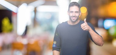 Hareketi el ile mutlu yaşasın yapıyor izole arka plan üzerinde kazak giyen genç yakışıklı adam. Başarı gösteren kameraya bakarak ifade onaylama.