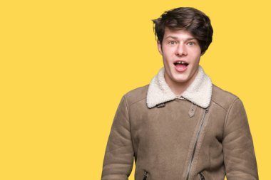 Yakışıklı delikanlı izole arka plan korkuyor ve şok sürpriz ifade, korku ve heyecan yüz üzerinden kış palto giyiyor.