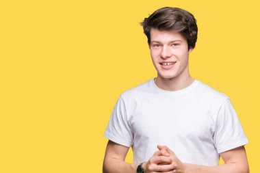 Arka plan eller üzerinde rahat beyaz t-shirt giyen genç yakışıklı adam birlikte izole ve rahat ve neşeli gülümseyen parmak çarpı işareti. Başarı ve iyimser