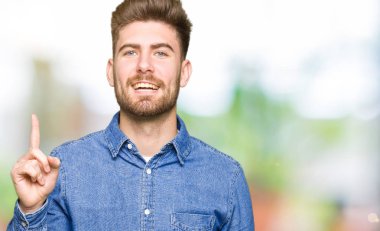 Genç yakışıklı sarışın adam başarılı bir fikir ile parmak işaret rahat kot gömlek giyiyor. Çıktı ve mutlu. Bir numara.